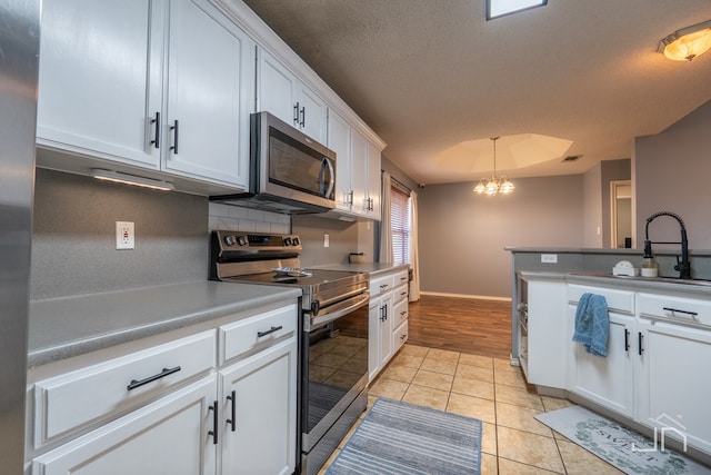 kitchen with light tile patterned flooring, decorative backsplash, white cabinets, appliances with stainless steel finishes, and a chandelier