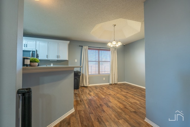 kitchen featuring a tray ceiling, stainless steel microwave, white cabinetry, an inviting chandelier, and dark wood-style flooring