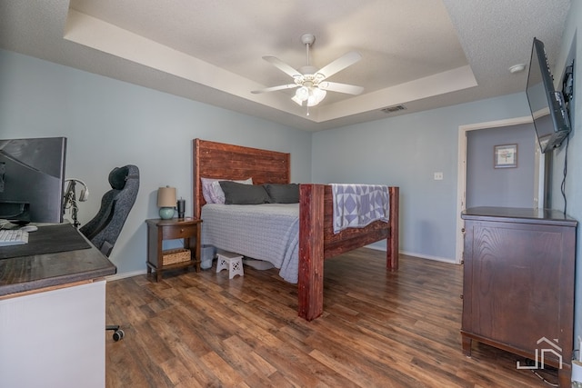 bedroom with visible vents, dark wood-style floors, baseboards, a raised ceiling, and ceiling fan