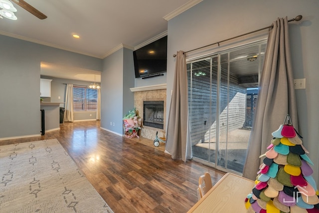 living area with a tiled fireplace, ceiling fan with notable chandelier, crown molding, and wood finished floors