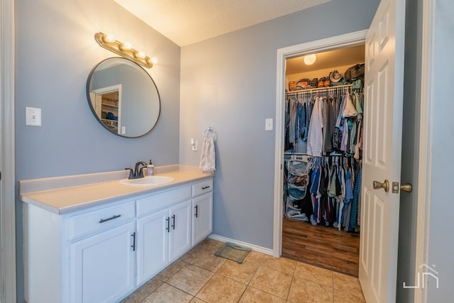 bathroom featuring tile patterned flooring, vanity, a walk in closet, and baseboards