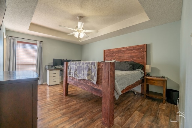 bedroom featuring a tray ceiling, wood finished floors, and a textured ceiling