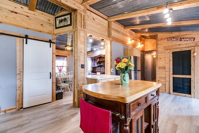 kitchen with wooden walls, light hardwood / wood-style floors, a barn door, and beamed ceiling