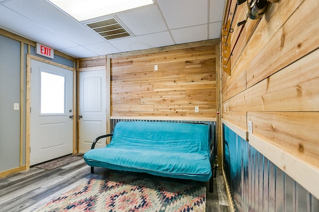 living area with wood-type flooring, a drop ceiling, and wood walls