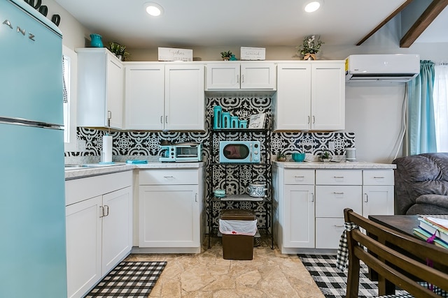 kitchen with an AC wall unit, fridge, white cabinets, and decorative backsplash