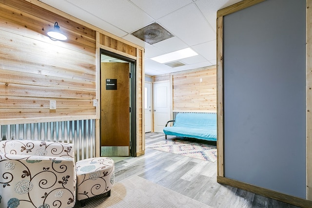 hall with wood-type flooring, wooden walls, and a drop ceiling