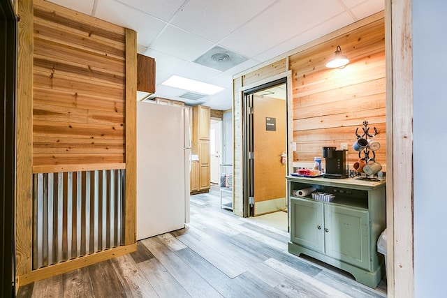 corridor featuring light hardwood / wood-style flooring, wooden walls, and a paneled ceiling