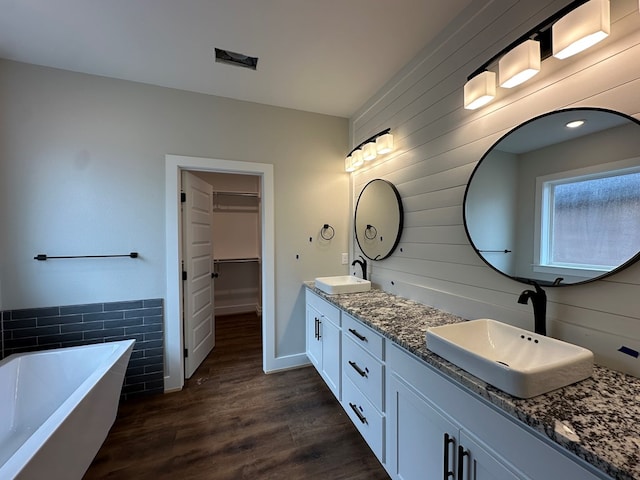 3611 Clearview Dr, San Angelo, TX 76904 - bathroom with double vanity, a freestanding tub, wood finished floors, a spacious closet, and tile walls