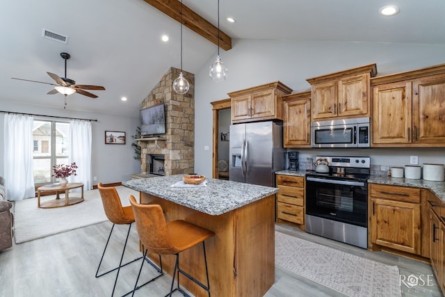 kitchen with visible vents, open floor plan, a center island, stainless steel appliances, and ceiling fan