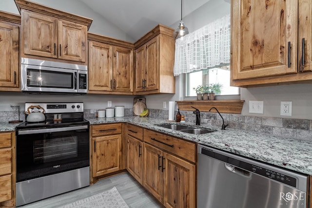 kitchen with a sink, lofted ceiling, appliances with stainless steel finishes, and light stone countertops