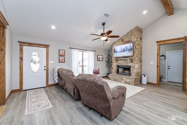 living room featuring visible vents, ceiling fan, beamed ceiling, a stone fireplace, and light wood-style flooring