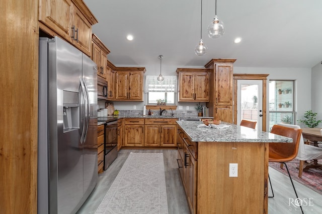 kitchen featuring a center island, light stone countertops, brown cabinets, a kitchen breakfast bar, and stainless steel appliances