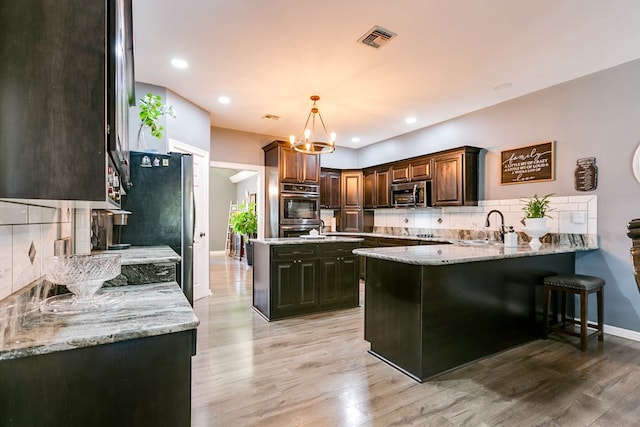 kitchen with light stone counters, hanging light fixtures, kitchen peninsula, and appliances with stainless steel finishes