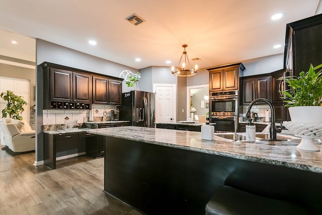 kitchen with appliances with stainless steel finishes, backsplash, hanging light fixtures, light hardwood / wood-style floors, and light stone countertops