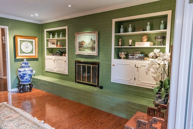 interior space featuring a brick fireplace, ornamental molding, built in features, and hardwood / wood-style floors