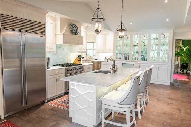 kitchen featuring white cabinetry, light stone counters, premium appliances, a center island with sink, and decorative backsplash