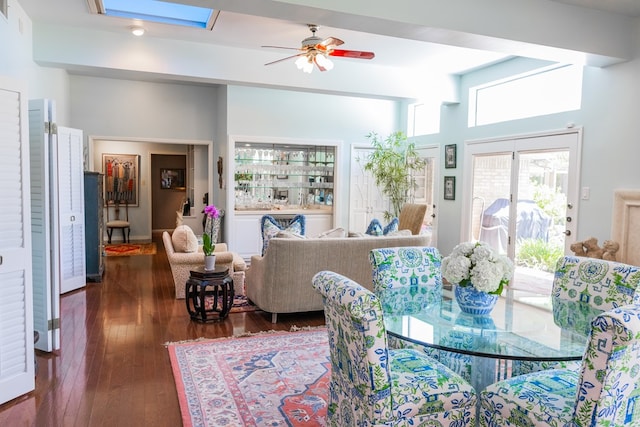 dining space with ceiling fan, dark hardwood / wood-style flooring, a skylight, and a towering ceiling