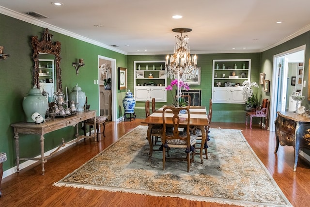 dining room featuring hardwood / wood-style flooring, crown molding, an inviting chandelier, and built in features