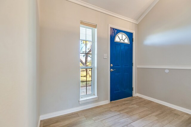 foyer entrance with ornamental molding, vaulted ceiling, and light hardwood / wood-style flooring