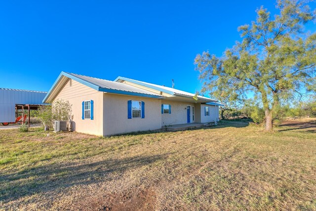 rear view of house featuring central AC unit and a lawn