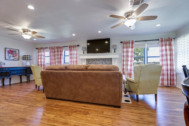 living area featuring light wood-style floors, ornamental molding, a ceiling fan, and visible vents