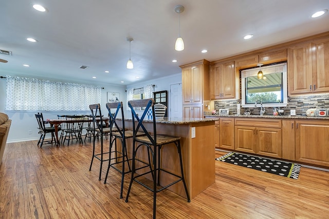kitchen with a sink, stone countertops, light wood-style flooring, decorative backsplash, and a kitchen bar