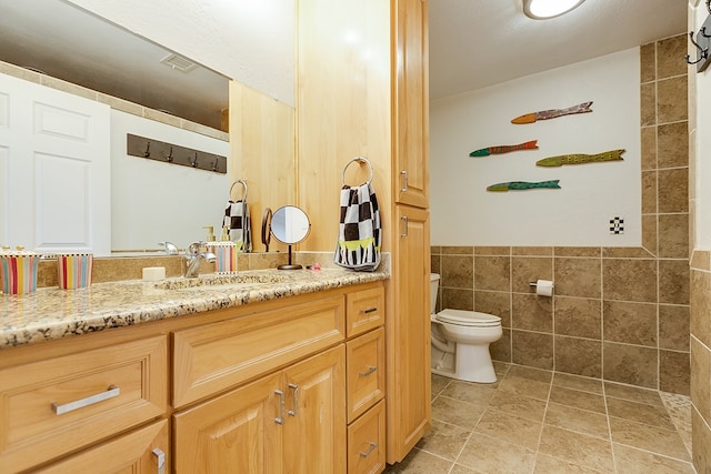 full bath featuring wainscoting, tile patterned flooring, vanity, toilet, and tile walls