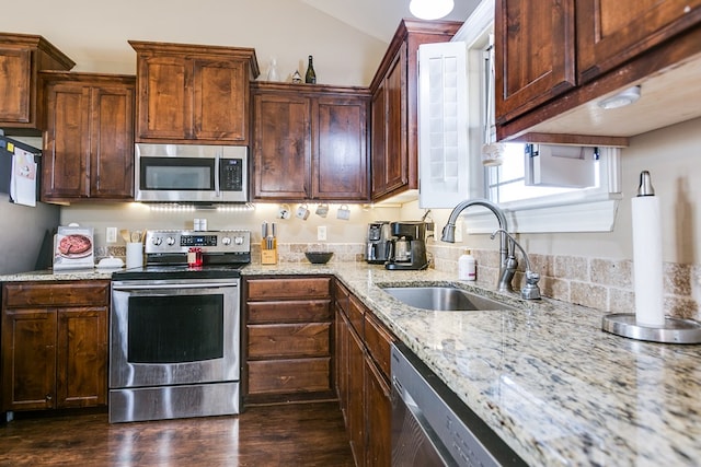 kitchen with appliances with stainless steel finishes, dark hardwood / wood-style floors, light stone countertops, and sink