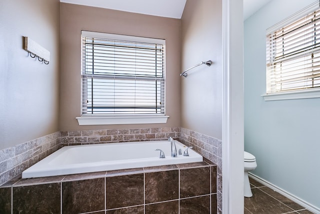 bathroom featuring a relaxing tiled tub, tile patterned floors, and toilet