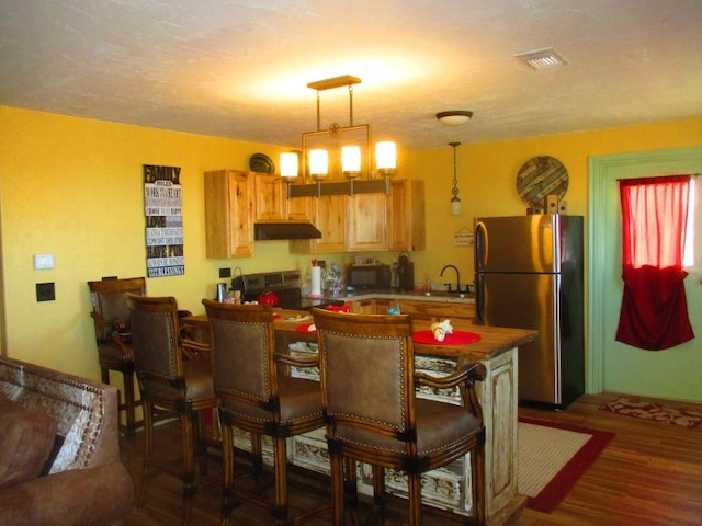 kitchen with a breakfast bar, decorative light fixtures, sink, stainless steel appliances, and dark wood-type flooring