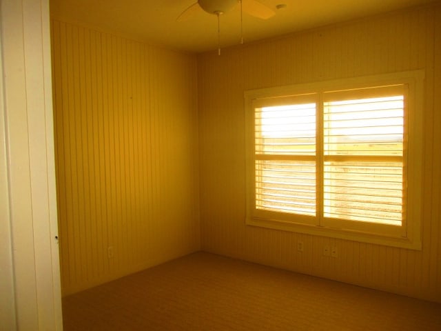 unfurnished room with ceiling fan and wood walls