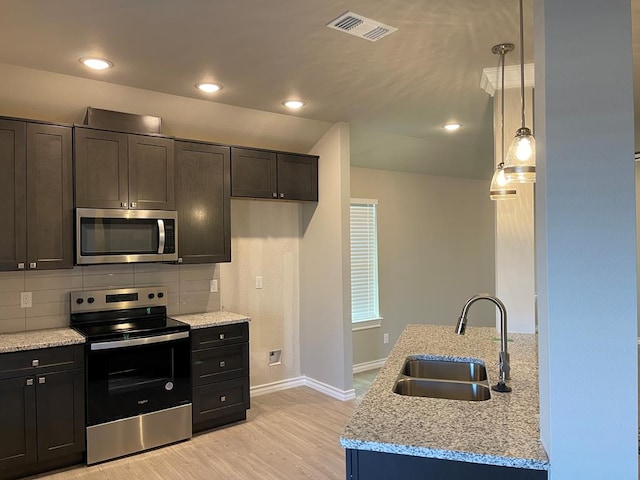 kitchen with pendant lighting, sink, stainless steel appliances, light stone counters, and light hardwood / wood-style floors