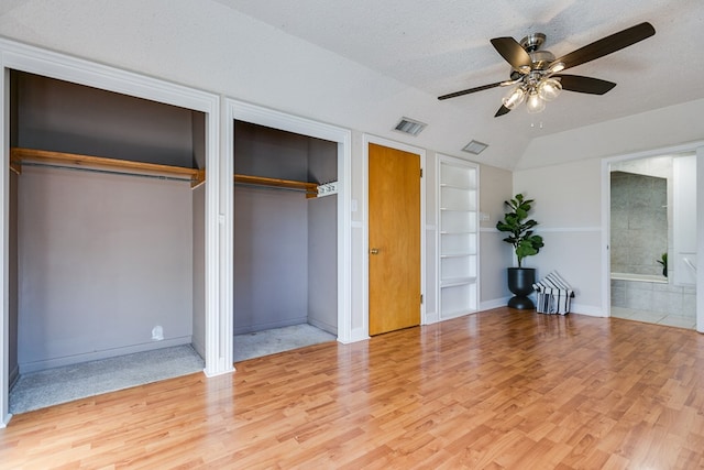 unfurnished bedroom with lofted ceiling, ceiling fan, wood-type flooring, a textured ceiling, and multiple closets