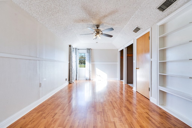 empty room with ceiling fan, a textured ceiling, light wood-type flooring, and built in shelves