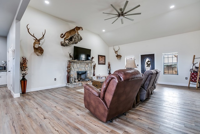 living room featuring lofted ceiling, a fireplace, light hardwood / wood-style flooring, and ceiling fan