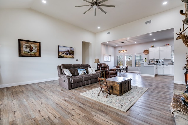 living room with ceiling fan, a high ceiling, and light wood-type flooring