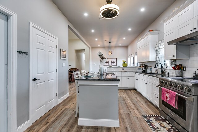 kitchen with white cabinetry, hanging light fixtures, light hardwood / wood-style flooring, stainless steel stove, and a kitchen island