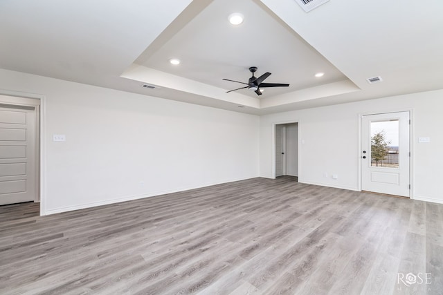 unfurnished living room featuring light wood finished floors, baseboards, and a tray ceiling