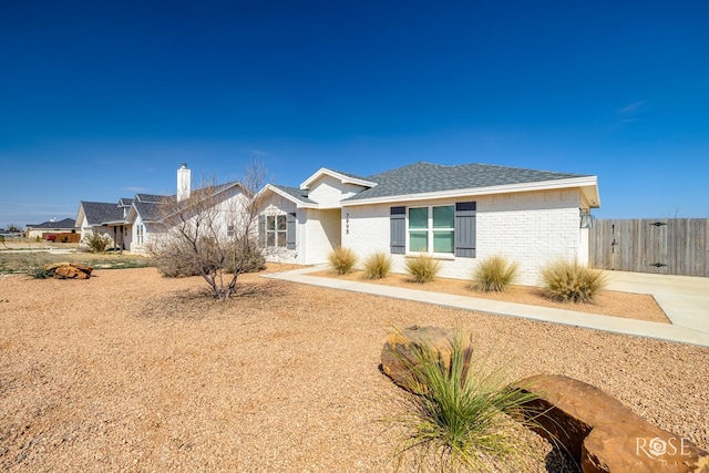 ranch-style home with a shingled roof, brick siding, and fence