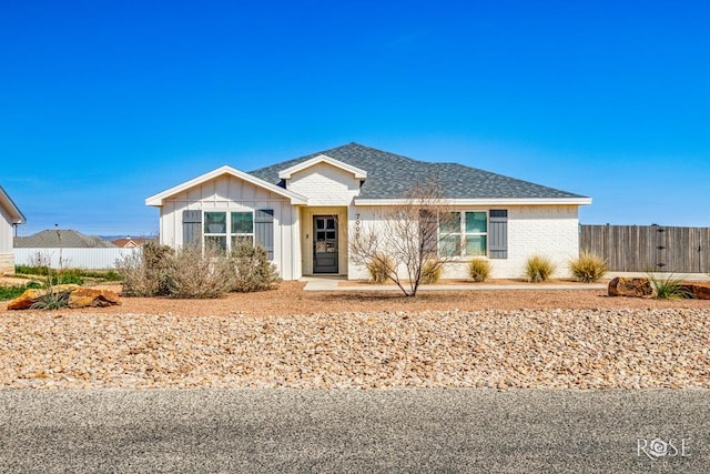 single story home featuring brick siding, board and batten siding, a shingled roof, and fence