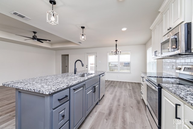 kitchen with visible vents, a tray ceiling, stainless steel appliances, white cabinetry, and a sink