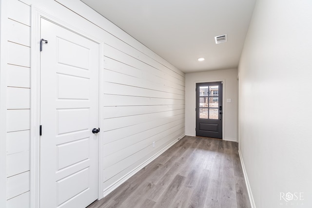 doorway to outside with light wood finished floors, visible vents, wooden walls, and baseboards