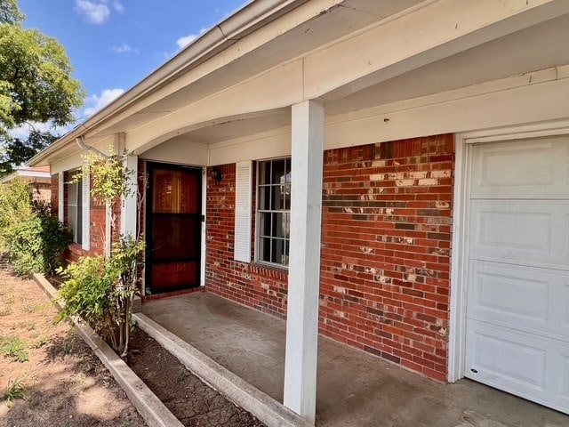 721 Spaulding St, San Angelo, TX 76903 - doorway to property featuring a garage, brick siding, and a porch