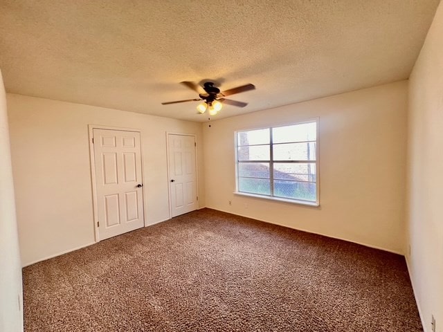 721 Spaulding St, San Angelo, TX 76903 - unfurnished bedroom with carpet flooring, a textured ceiling, a ceiling fan, and multiple closets