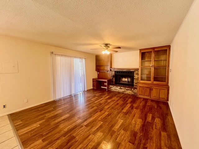721 Spaulding St, San Angelo, TX 76903 - unfurnished living room featuring dark wood finished floors, ceiling fan, a textured ceiling, a fireplace, and built in shelves