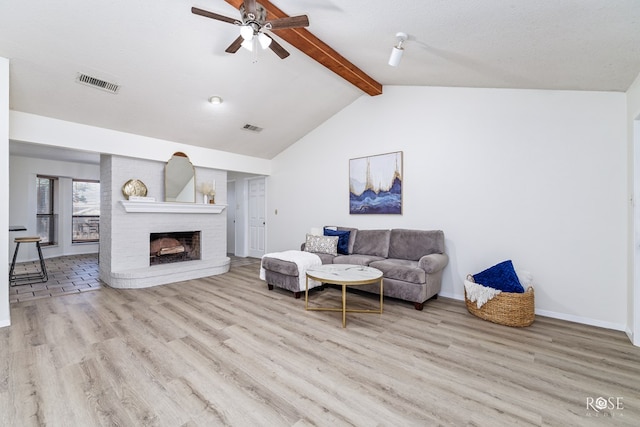 living room with lofted ceiling with beams, a brick fireplace, a textured ceiling, ceiling fan, and light hardwood / wood-style floors