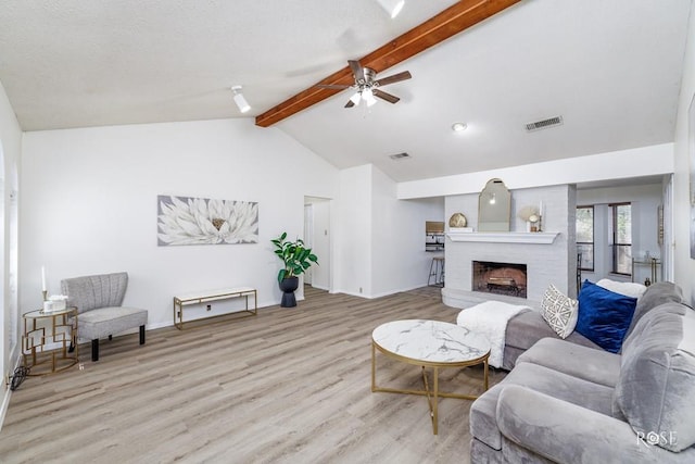 living room with ceiling fan, a fireplace, lofted ceiling with beams, and light hardwood / wood-style flooring