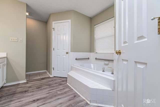 bathroom with baseboards, wood finished floors, a textured ceiling, vanity, and a bath