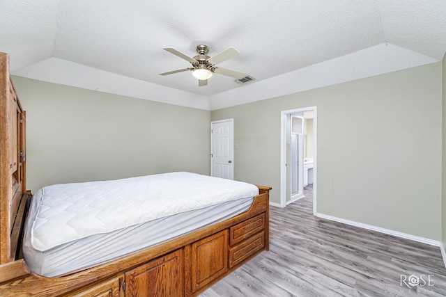 bedroom featuring a textured ceiling, light wood-style flooring, visible vents, baseboards, and vaulted ceiling