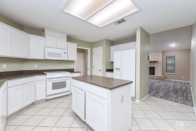 kitchen featuring a center island, light tile patterned floors, visible vents, white cabinetry, and white appliances